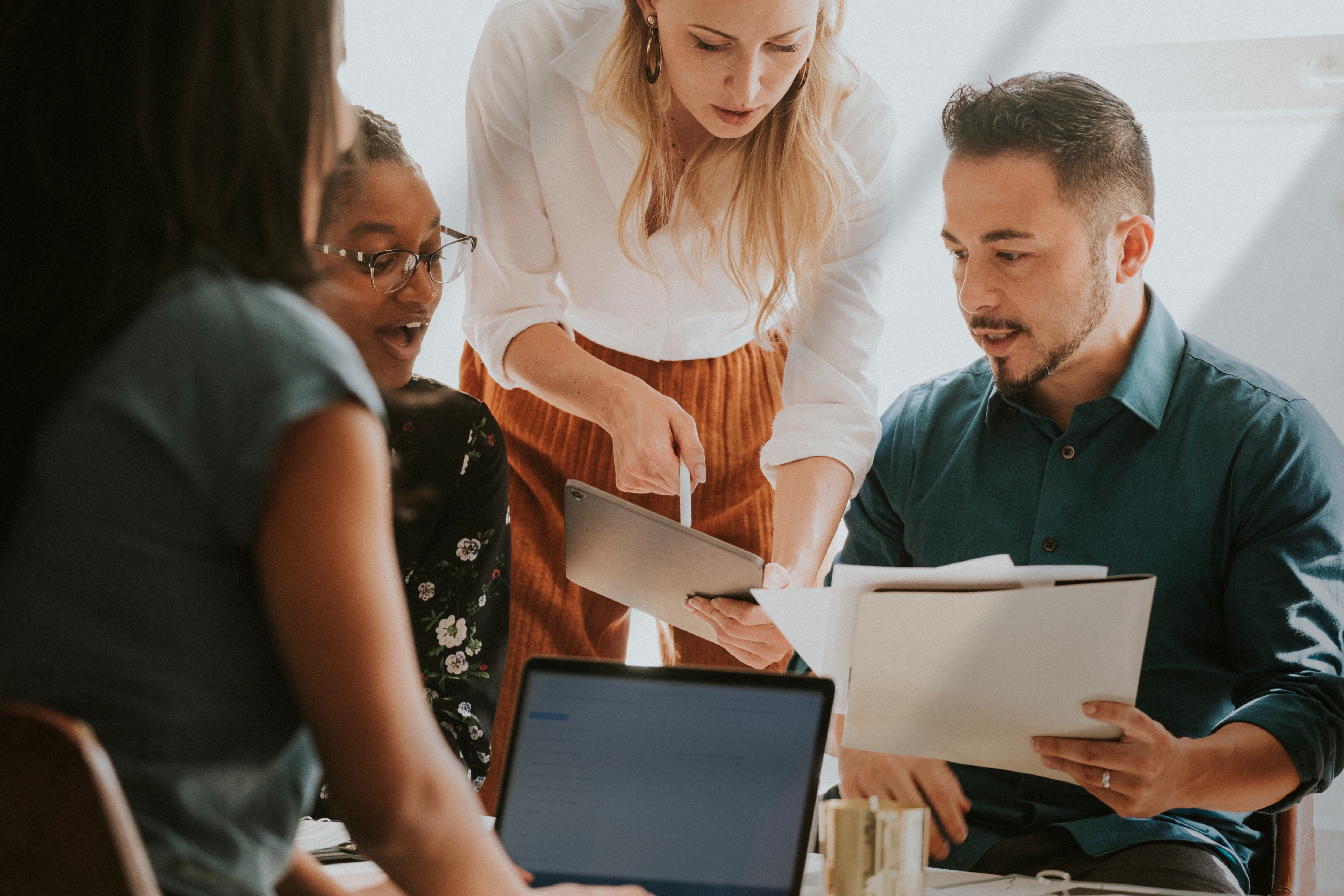 Group of colleagues collaborating with a tablet, laptop, and documents in an office setting.