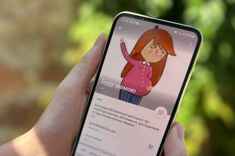 A photo shows hands holding a smartphone that displays the "I'll Be a Mother" chatbot.